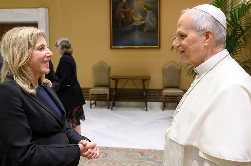 woman with blond hair in a black dress suit conversing with the Pope
