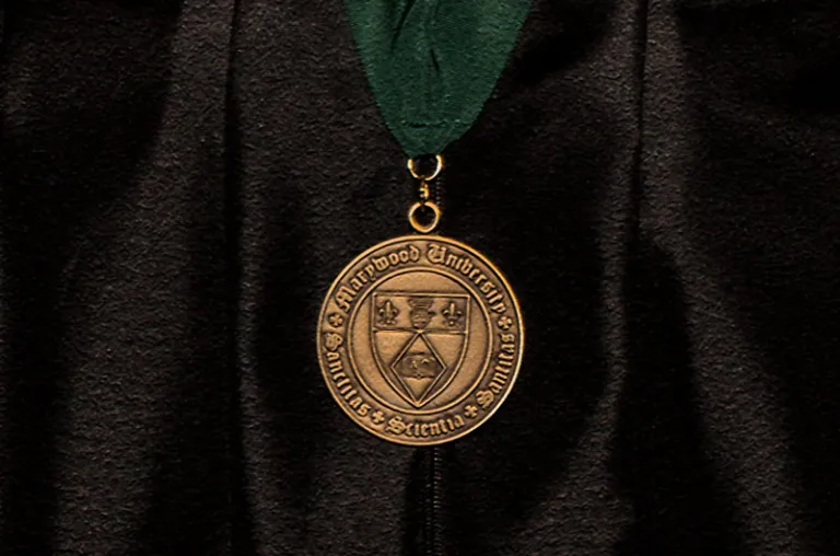 Gold Medal with Marywood seal hanging from a green ribbon against black academic attire