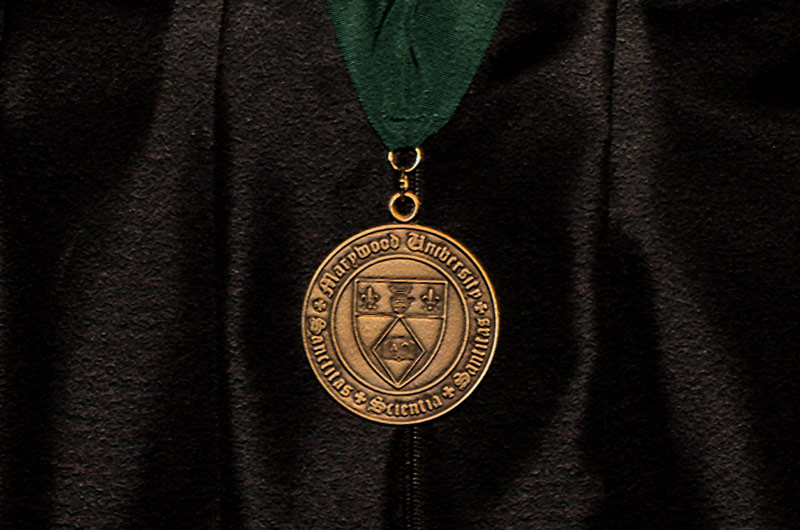 Gold Medal with Marywood seal hanging from a green ribbon against black academic attire