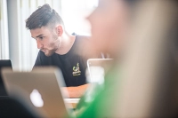 focused on guy staring intently at computer screen with blurred images of other students and laptops in front of him From Wealth Management to Fraud Prevention: Careers in Finance & Crime Investigation