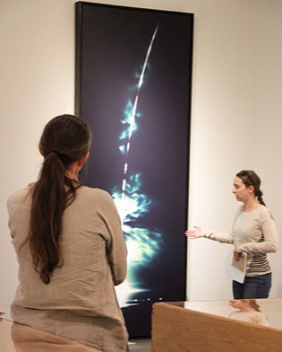 woman looking at artwork on wall in gallery and student giving presentation