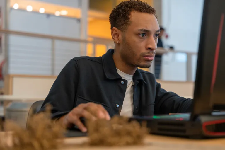 male student sitting at desk staring intently at computer and using mouse to click